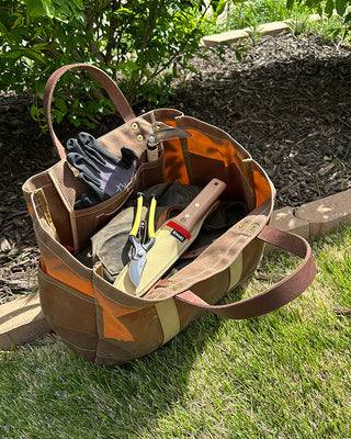 Waxed canvas tool tote in a garden bed, holding hand tools and gloves