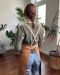Person modeling a cross-back strap copper ceramics potter apron in a studio. 